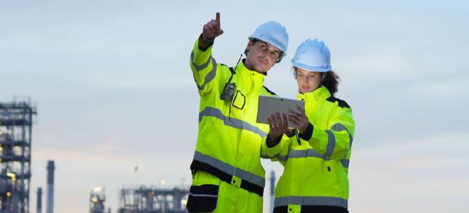 Two safety engineers reviewing project documentation in front of a petrochemical plant