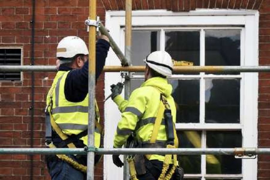 Two scaffolders in high-visibility clothing erecting a scaffold structure